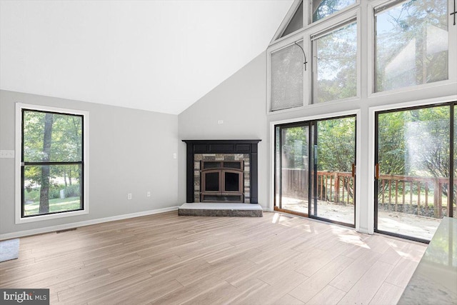 unfurnished living room with a stone fireplace, light hardwood / wood-style floors, and a high ceiling