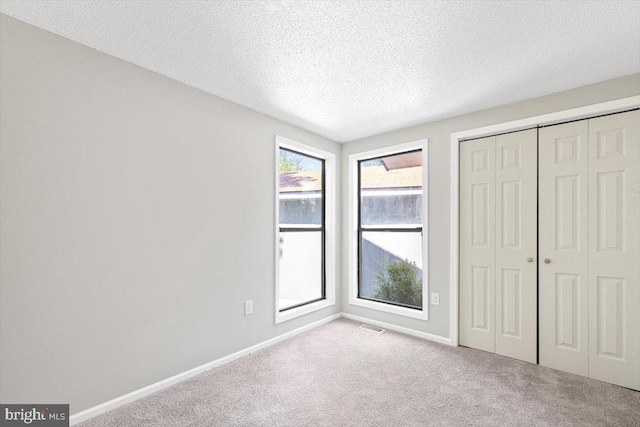 unfurnished bedroom with light colored carpet, a textured ceiling, and a closet