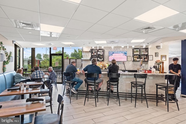 interior space with a drop ceiling, light wood-type flooring, floor to ceiling windows, and bar area