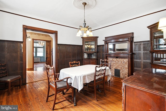 dining space with radiator, a fireplace, a chandelier, and wainscoting