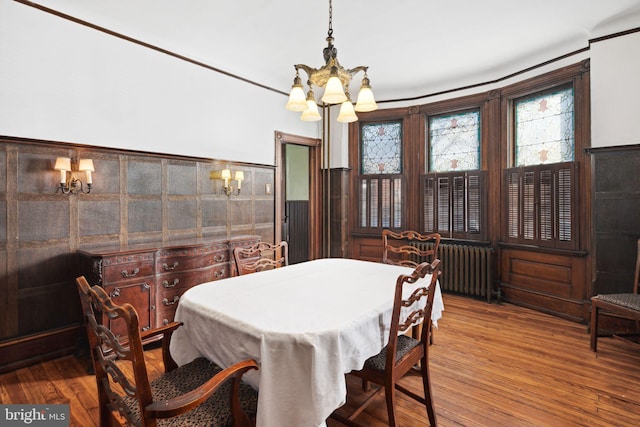 dining space with wood finished floors, wainscoting, radiator heating unit, and an inviting chandelier