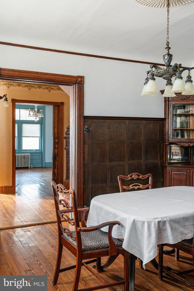 dining area featuring radiator heating unit, ornamental molding, a notable chandelier, and wood finished floors