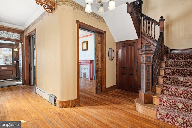 entrance foyer with ornamental molding, a baseboard radiator, an inviting chandelier, and wood finished floors