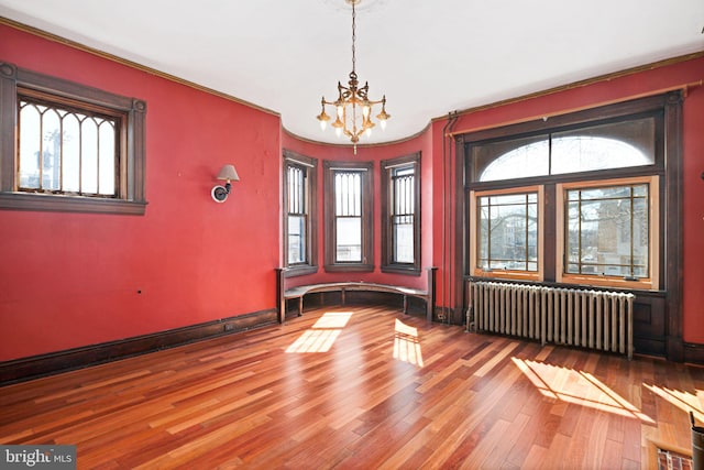 empty room with baseboards, radiator heating unit, wood finished floors, and a notable chandelier