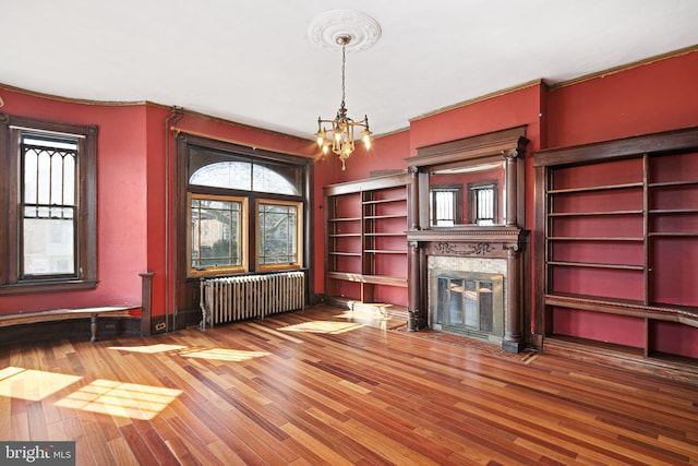 unfurnished living room featuring a fireplace with flush hearth, radiator, a healthy amount of sunlight, and wood finished floors