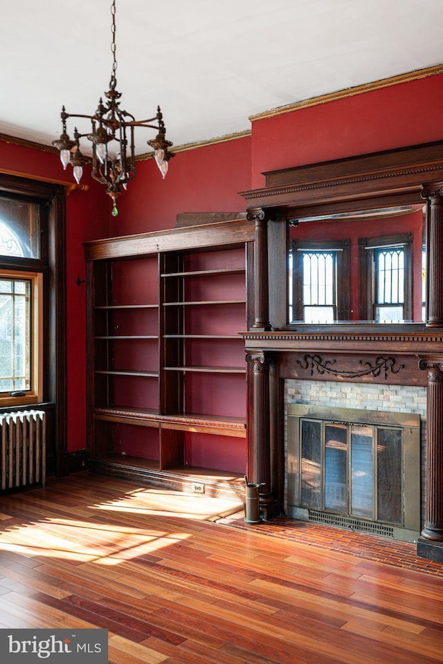 unfurnished living room featuring a brick fireplace, an inviting chandelier, radiator heating unit, and wood finished floors