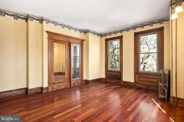 spare room featuring dark wood-style flooring, radiator heating unit, and baseboards