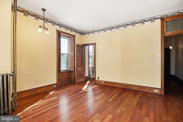 unfurnished room with an inviting chandelier, baseboards, radiator heating unit, and wood finished floors