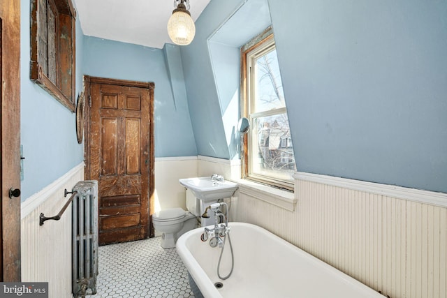 bathroom featuring radiator, toilet, a freestanding bath, and wainscoting