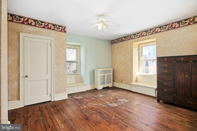 unfurnished bedroom featuring dark wood-style floors, multiple windows, baseboards, and wallpapered walls