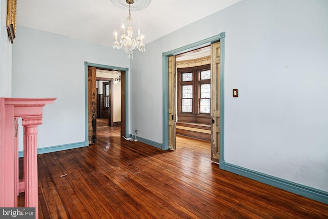 unfurnished dining area with a notable chandelier, dark wood finished floors, and baseboards