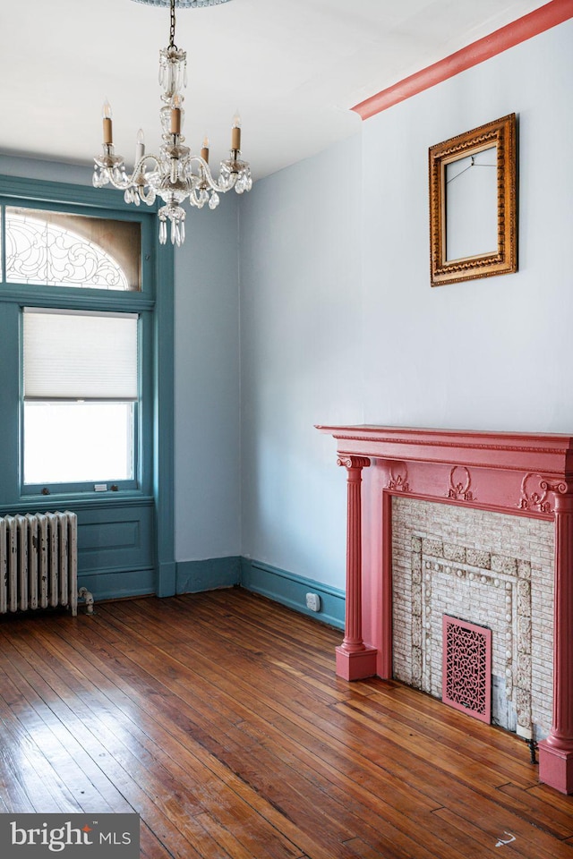 unfurnished living room with a fireplace, radiator, an inviting chandelier, dark wood-type flooring, and baseboards