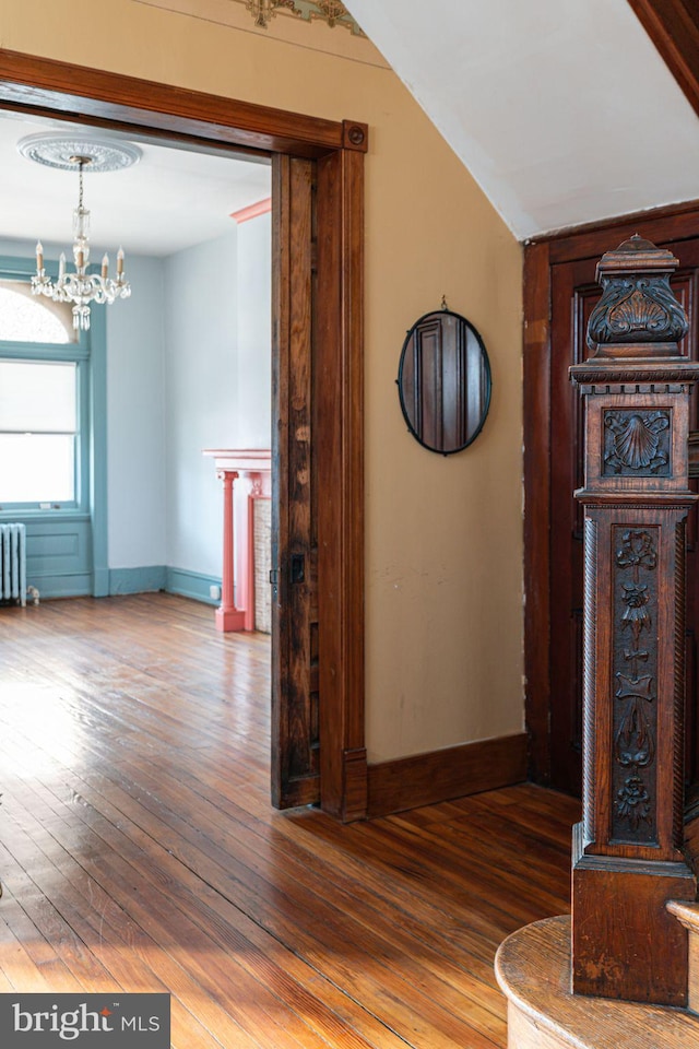 corridor with a chandelier, baseboards, radiator heating unit, and wood finished floors