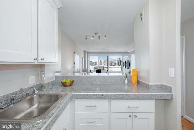 kitchen with white cabinetry, kitchen peninsula, sink, and light stone counters