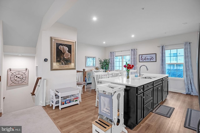 kitchen featuring stainless steel dishwasher, sink, a kitchen island with sink, and light wood-type flooring