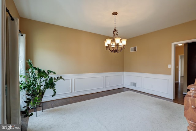 spare room featuring an inviting chandelier, visible vents, wood finished floors, and wainscoting