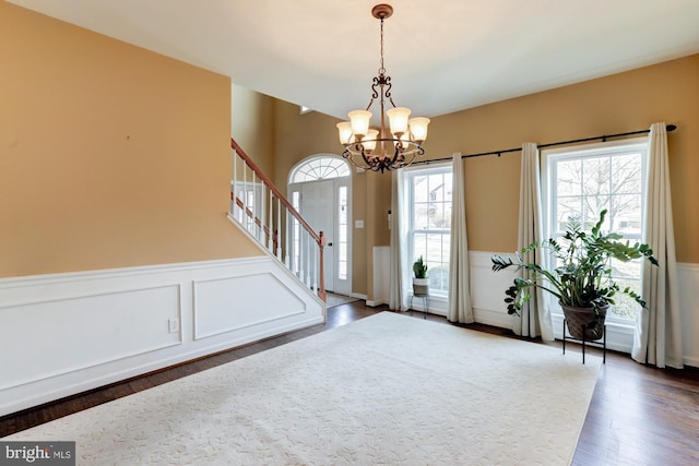 entryway featuring a wainscoted wall, dark wood-type flooring, stairway, and a chandelier