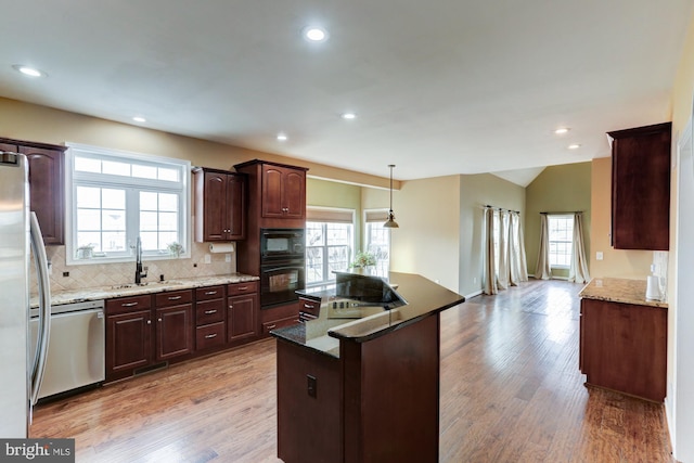 kitchen featuring light wood-style flooring, dark stone countertops, decorative light fixtures, black appliances, and a sink