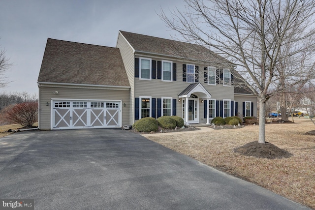 colonial house with a garage, aphalt driveway, and roof with shingles