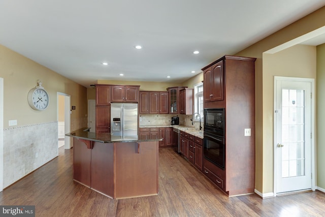 kitchen featuring a kitchen island, glass insert cabinets, a breakfast bar, dark stone countertops, and black appliances