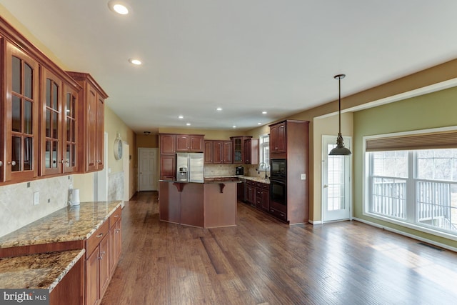 kitchen featuring light stone counters, hanging light fixtures, stainless steel refrigerator with ice dispenser, dark wood finished floors, and glass insert cabinets