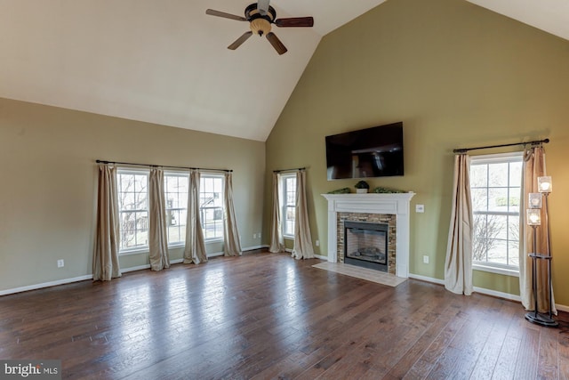 unfurnished living room featuring baseboards, dark wood-style floors, ceiling fan, a stone fireplace, and high vaulted ceiling