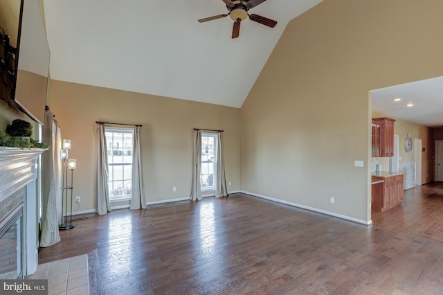 unfurnished living room with baseboards, a ceiling fan, a fireplace with flush hearth, dark wood-type flooring, and high vaulted ceiling