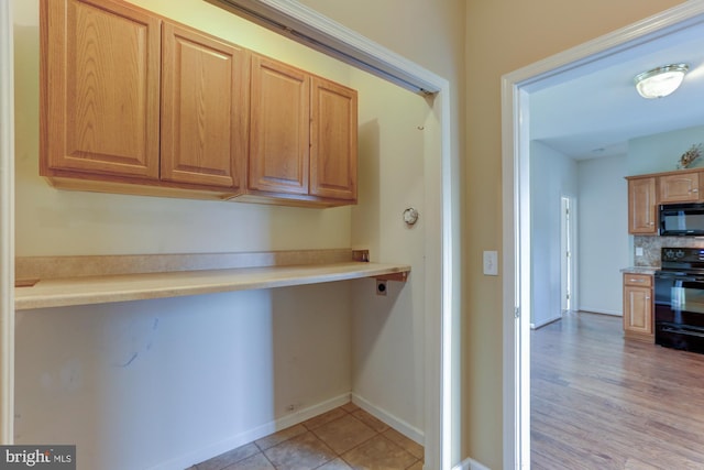 kitchen featuring built in desk, light countertops, decorative backsplash, black appliances, and baseboards