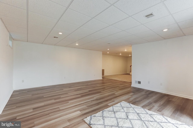 below grade area featuring baseboards, a drop ceiling, visible vents, and light wood-style floors