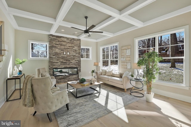 living room with a healthy amount of sunlight, a stone fireplace, coffered ceiling, and light hardwood / wood-style floors