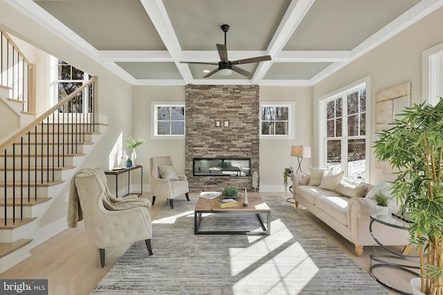 living room featuring coffered ceiling, a stone fireplace, light wood-type flooring, beamed ceiling, and ceiling fan