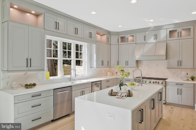 kitchen featuring sink, dishwasher, range hood, light hardwood / wood-style floors, and a center island with sink