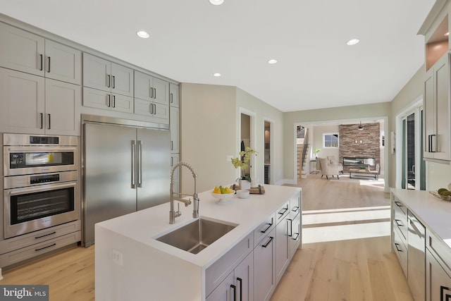 kitchen with gray cabinets, appliances with stainless steel finishes, sink, a kitchen island with sink, and light hardwood / wood-style floors