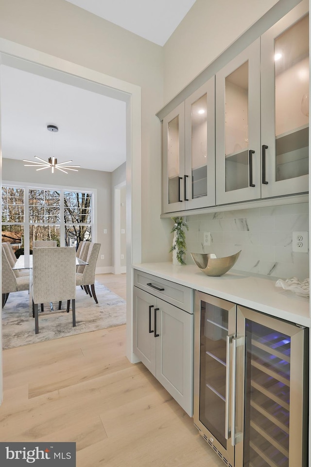 bar featuring ceiling fan, gray cabinetry, backsplash, wine cooler, and light wood-type flooring