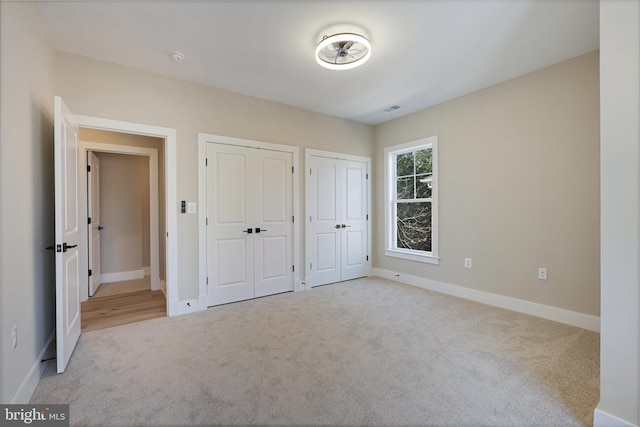 unfurnished bedroom with multiple closets and light carpet