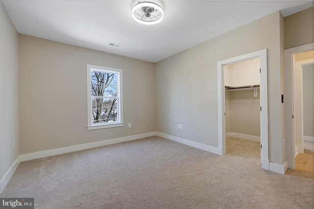 unfurnished bedroom featuring light carpet, a walk in closet, and a closet