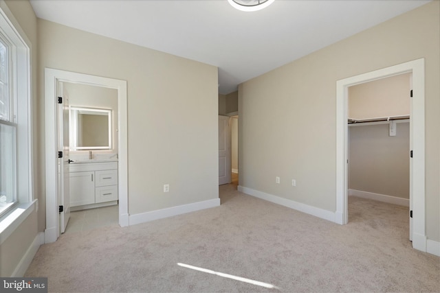 unfurnished bedroom with light colored carpet, ensuite bathroom, a spacious closet, and a closet