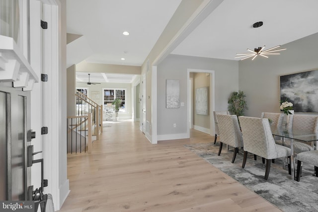 foyer entrance featuring beam ceiling, coffered ceiling, a chandelier, and light hardwood / wood-style flooring