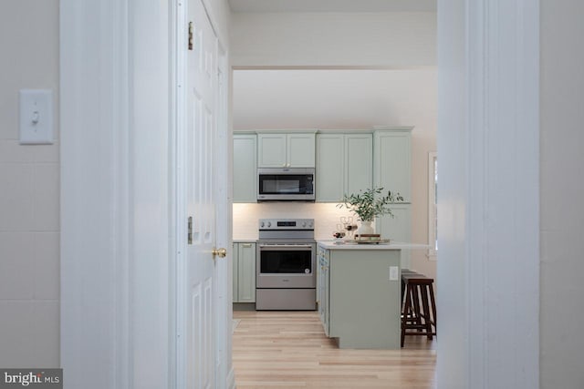 kitchen with stainless steel appliances, tasteful backsplash, a breakfast bar area, and light hardwood / wood-style flooring