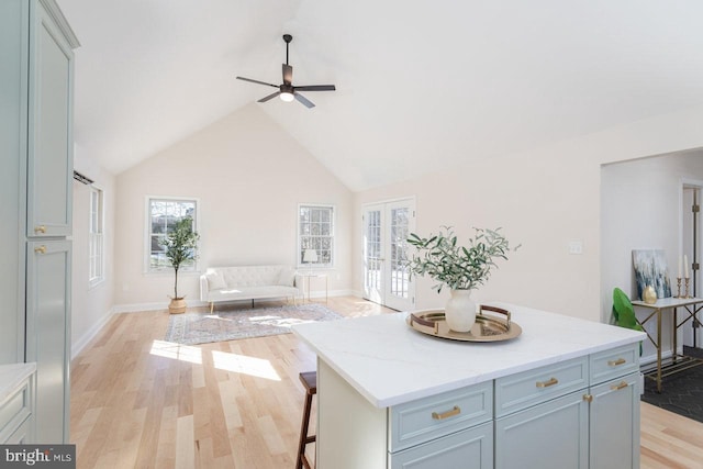 kitchen with light hardwood / wood-style flooring, a breakfast bar, high vaulted ceiling, a center island, and light stone countertops