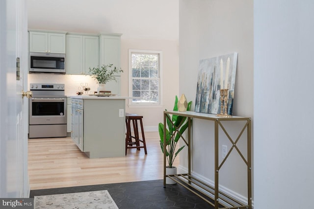 kitchen featuring appliances with stainless steel finishes, a breakfast bar, backsplash, kitchen peninsula, and light wood-type flooring