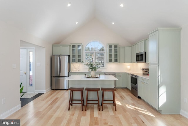 kitchen featuring a breakfast bar area, appliances with stainless steel finishes, backsplash, a center island, and light wood-type flooring