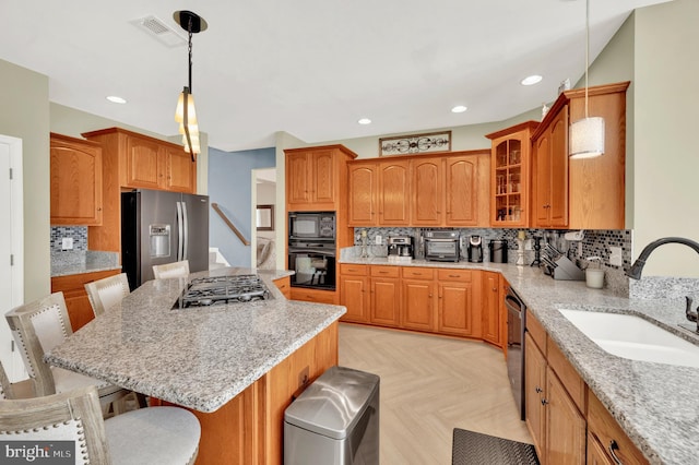 kitchen featuring decorative light fixtures, glass insert cabinets, a sink, a kitchen breakfast bar, and black appliances