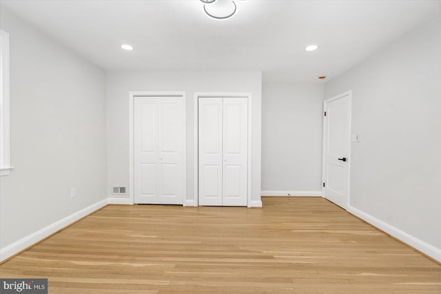 unfurnished bedroom with light hardwood / wood-style floors and multiple closets