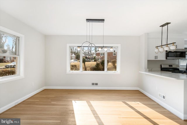 unfurnished dining area featuring plenty of natural light, a notable chandelier, and light wood-type flooring