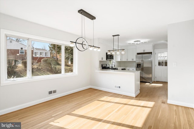 kitchen featuring decorative light fixtures, light hardwood / wood-style flooring, kitchen peninsula, stainless steel appliances, and white cabinets