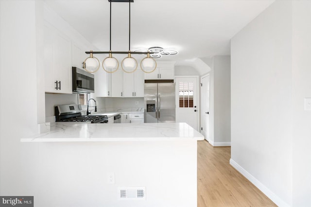 kitchen with hanging light fixtures, stainless steel appliances, light stone counters, white cabinets, and kitchen peninsula