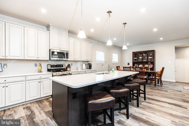 kitchen featuring sink, appliances with stainless steel finishes, white cabinetry, an island with sink, and decorative light fixtures