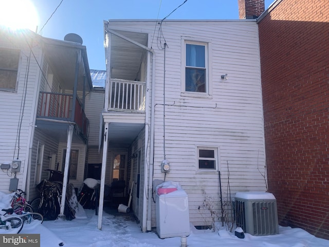 snow covered rear of property featuring cooling unit and a balcony