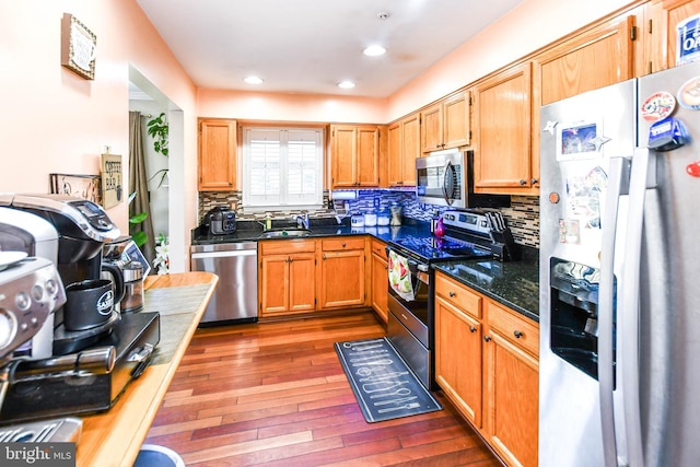 kitchen featuring sink, dark wood-type flooring, appliances with stainless steel finishes, tasteful backsplash, and dark stone counters